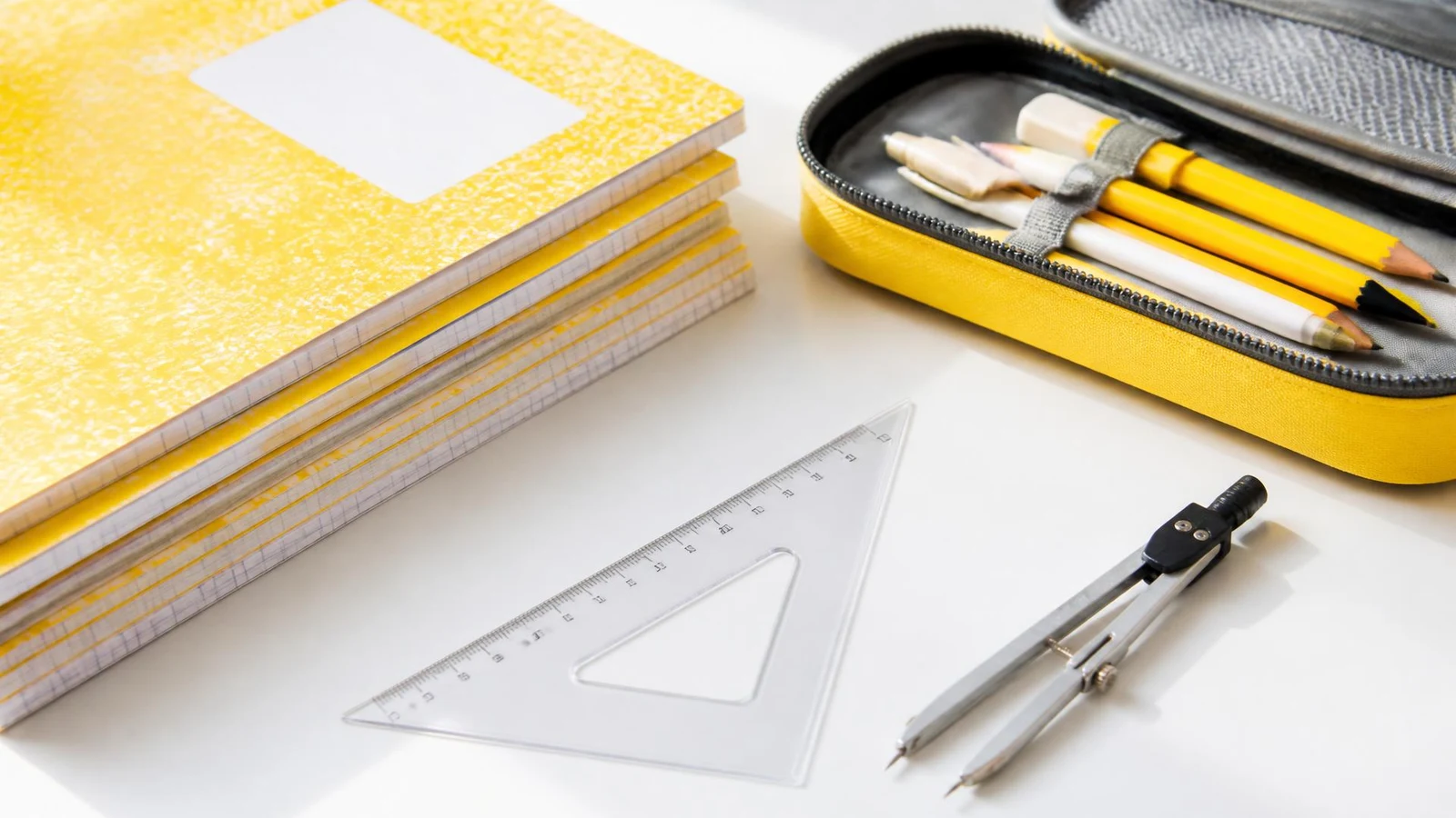 Cahiers, trousse et instruments de géométrie posés sur un bureau clair