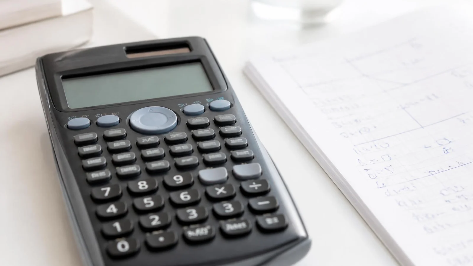 Calculatrice scientifique posée près d'un cahier de brouillon sur un bureau clair